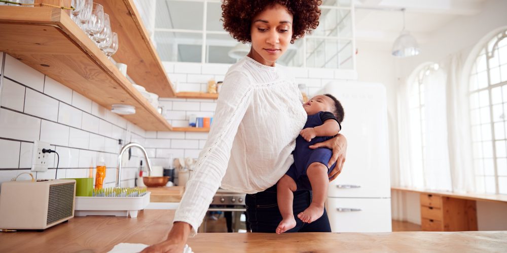 Multi-Tasking Mother Holds Sleeping Baby Son And Cleans In Kitchen
